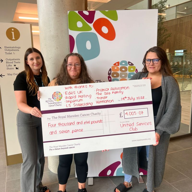 Three women proudly holding a check in front of a building to support a local Social Club.